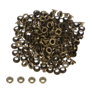 Könnte beinhalten: Ein Haufen antiker, messingfarbener Ösen, von denen einige unten in einer Reihe angeordnet sind. Diese Metallbefestigungen haben eine kreisförmige Form mit einem Loch in der Mitte und werden zur Verstärkung von Löchern in Stoff oder Leder verwendet. Die Ösen haben einen Durchmesser von etwa 0,6 cm.