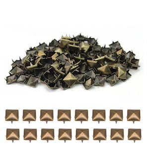 Può includere: Una collezione di borchie metalliche a forma di piramide color bronzo, con basi a quattro punte. Alcune borchie sono sparse in un mucchio, mentre altre sono disposte ordinatamente in file. Queste borchie decorative sono ideali per progetti di artigianato.
