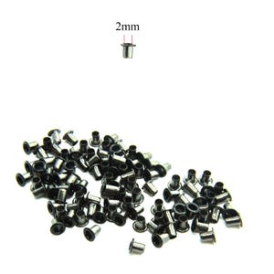 Könnte beinhalten: Eine Ansammlung kleiner, dunkelgrauer Metallösen, jede mit einer Öffnung von 2 mm. Die Ösen sind auf weißem Hintergrund verstreut, wobei einige aufrecht und andere auf der Seite liegen. Sie werden häufig für Bastelarbeiten und Lederarbeiten verwendet.