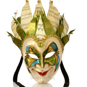 May include: A colorful Venetian masquerade mask with a green, gold, and blue design. The mask has a smiling face and a tall, pointed crown decorated with musical notes.