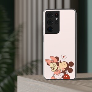 Op de afbeelding: Een witte telefoonhoes met een roze en bruine cartoon afbeelding van Mickey Mouse en Minnie Mouse die elkaar kussen. De hoes heeft een zwarte camera-uitstulping met drie lenzen.