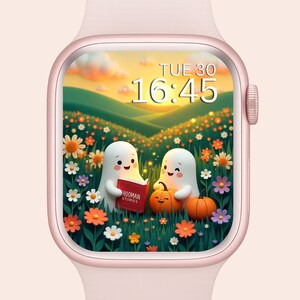 Peut inclure: Un Apple Watch rose doré affiche une scène fantaisiste. Deux fantômes de dessins animés lisent un livre intitulé "HOOMAN STORIES" près de citrouilles et de fleurs. L'heure est 16h45 le mardi. L'arrière-plan montre un coucher de soleil sur des collines verdoyantes.