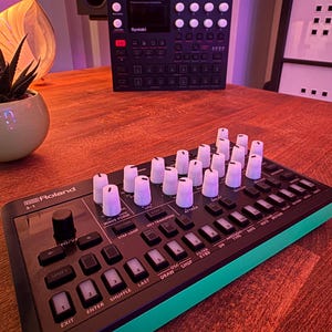 Könnte beinhalten: Ein schwarzer und grüner Roland 5-1 Synthesizer mit weißen Knöpfen und einem kleinen Bildschirm. Der Synthesizer verfügt über eine Vielzahl von Knöpfen und Bedienelementen, darunter eine Shift-Taste, eine Waveform-Taste, eine Pattern-Taste, eine Step-Taste, eine Loop-Taste, eine Key-Transpose-Taste, eine Attack-Taste, eine OSC-Taste, eine Draw-Taste, eine Chop-Taste, eine Filter-Taste, eine Kyed-Taste, eine On-Taste, eine Arpeggio-Taste, eine Note-Taste und eine Motion-Taste.