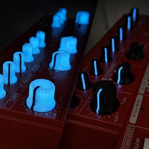 Könnte beinhalten: Ein rotes Bedienfeld für einen elektronischen Musik-Synthesizer mit zwei Knopf-Sets. Die linke Seite besteht aus durchscheinenden, blau leuchtenden Knöpfen, während die rechte Seite schwarze Knöpfe mit dünnen, vertikalen blauen Lichtstreifen zeigt.
