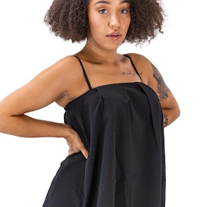 May include: A woman wearing a black sleeveless top with a square neckline and a pleated bodice. She is wearing blue jeans with distressed details.