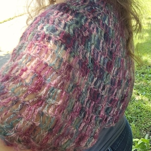 Peut inclure: Un châle tricoté à la main dans des tons de rose, de bleu et de vert. Le motif ajouré crée un aspect texturé et aéré. Le châle est drapé sur les épaules, mettant en valeur le motif complexe et les variations de couleurs. Le fil semble doux et légèrement flou.
