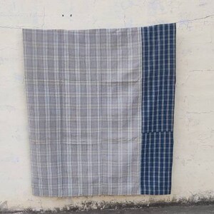 May include: A gray and blue plaid throw blanket with a blue border. The blanket is hanging on a white wall.