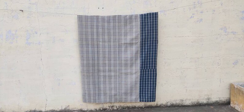 May include: A gray and blue plaid throw blanket with a blue border. The blanket is hanging on a white wall.