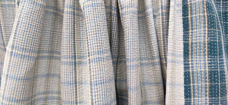 May include: Close-up of four fabric swatches with a blue and white plaid pattern. The fabric is woven with a subtle texture.