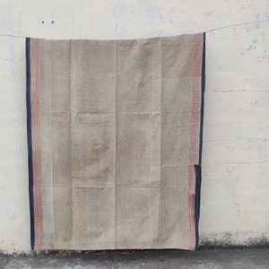 May include: A beige woven rug with a dark blue and red border hanging on a white wall.