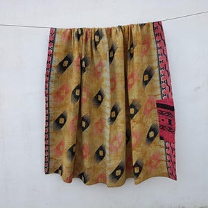 May include: A decorative textile hanging from a wire, featuring a repeating pattern of black, pink, and yellow diamond shapes. The edges are trimmed with a pink border. The textile is likely a blanket or throw.