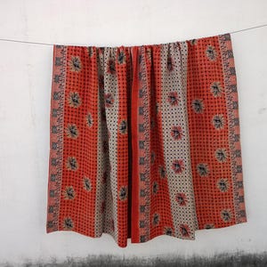 May include: A red and white kantha quilt with a floral pattern. The quilt is hanging on a white wall.