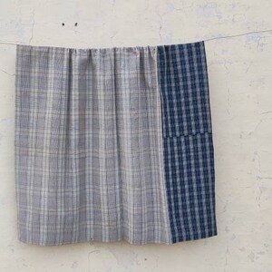 May include: A gray and white plaid fabric panel is sewn to a blue and white plaid fabric panel. The fabric is hanging on a clothesline.