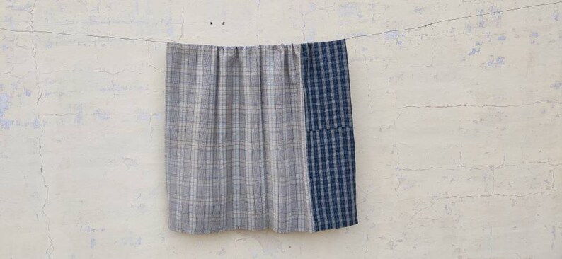 May include: A gray and white plaid fabric panel is sewn to a blue and white plaid fabric panel. The fabric is hanging on a clothesline.