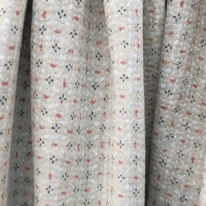 May include: Close-up of a beige fabric with a repeating pattern of small red and black shapes. The fabric has a textured, slightly bumpy surface.