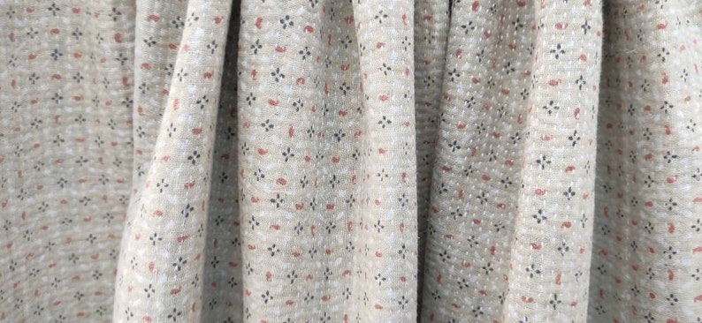 May include: Close-up of a beige fabric with a repeating pattern of small red and black shapes. The fabric has a textured, slightly bumpy surface.