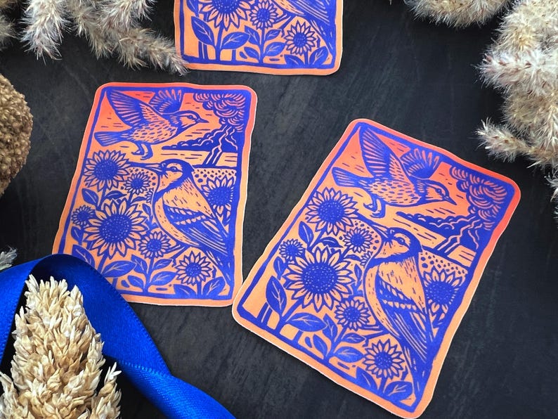 May include: Rectangular stickers with a blue and orange design. The stickers feature a bird, sunflowers, and a landscape. The bird is depicted in flight and perched among the sunflowers. The background is orange, and the design is blue.
