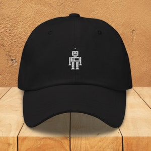 Puede incluir: Una gorra de béisbol negra con un diseño de robot bordado en blanco.