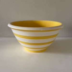 May include: A yellow mixing bowl with white stripes. The bowl is made of ceramic and has a smooth, glossy finish.