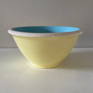 May include: A yellow ceramic bowl with a light blue interior and a white rim. The bowl has a rounded shape and sits on a white surface. This kitchenware item is suitable for mixing or serving.