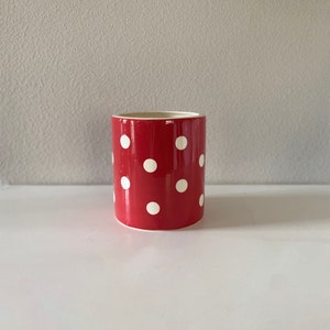 May include: A red ceramic pot with white polka dots. The pot is cylindrical in shape and has a smooth, glossy finish.