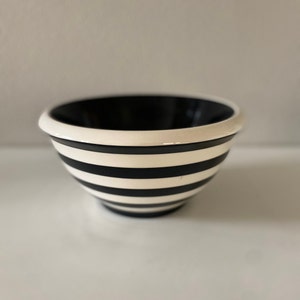 May include: A small white bowl with black stripes. The bowl is made of ceramic and has a glossy finish.