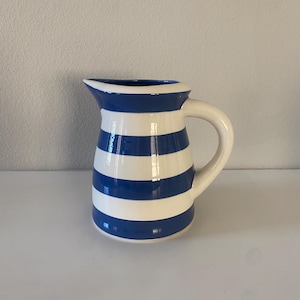 May include: A blue and white striped ceramic pitcher. The pitcher has a rounded body and a handle.