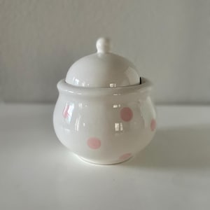 May include: White ceramic sugar bowl with a pink polka dot pattern and a lid.