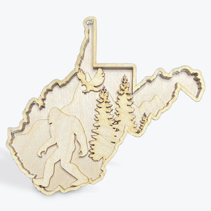 May include: A wooden cutout of the state of West Virginia with a silhouette of Bigfoot, a bird, and pine trees inside the state outline.