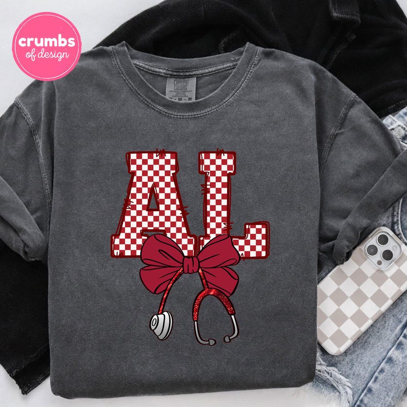 May include: Dark gray sweatshirt with the letters "AL" in a red and white checkered pattern. A red bow and stethoscope graphic are centered below the letters. A phone case with a checkered pattern is visible.