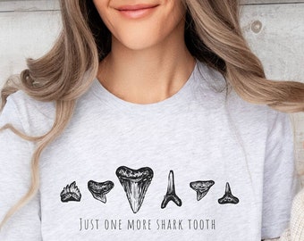 Puede incluir: Una camiseta gris jaspeada con una línea de ilustraciones de dientes de tiburón y el texto "Just one more shark tooth".