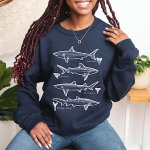 May include: A navy blue sweatshirt with a white graphic of four different shark silhouettes and their teeth. The text below each shark reads "White Shark", "Bull Shark", "Great White Shark", and "Sand Tiger Shark".