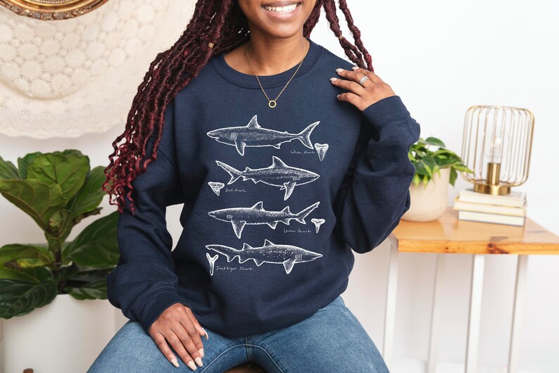 May include: A navy blue sweatshirt with a white graphic of four different shark silhouettes and their teeth. The text below each shark reads "White Shark", "Bull Shark", "Great White Shark", and "Sand Tiger Shark".