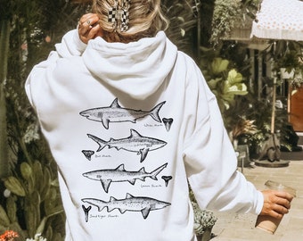 May include: White hoodie with a black and white illustration of four different types of sharks on the back. The sharks are labeled "White Shark", "Bull Shark", "Lemon Shark", and "Sand Tiger Shark".
