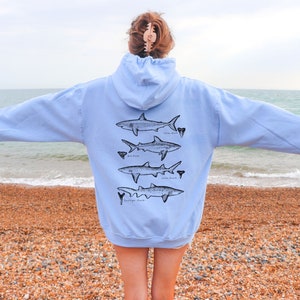 May include: A light blue hoodie with a graphic of five different types of sharks on the back. The sharks are labeled with their names: White Shark, Bull Shark, Lemon Shark, Sand Tiger Shark, and Dogfish Shark.