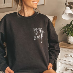 May include: Black sweatshirt with a white graphic of a shark and the text "Respect the Locals".