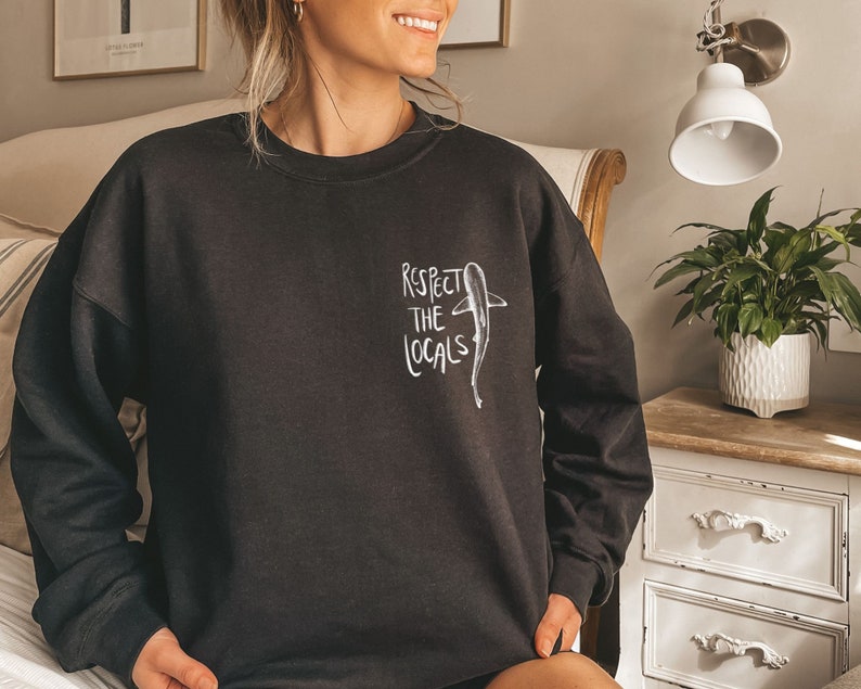May include: Black sweatshirt with a white graphic of a shark and the text "Respect the Locals".