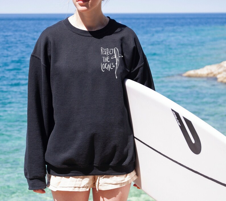 May include: A black sweatshirt with a white graphic of a shark and the text "Respect the Locals".