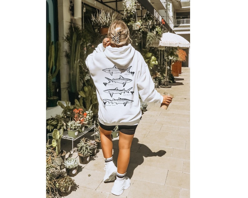 May include: White hoodie with a graphic of four different types of sharks on the back. The hoodie has a drawstring hood and a kangaroo pocket.