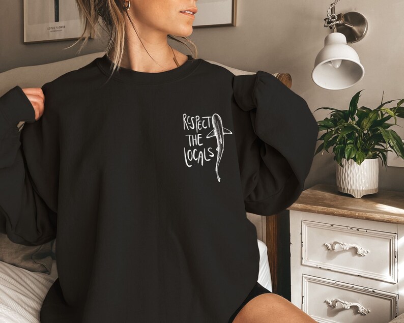 May include: Black sweatshirt with a white graphic of a shark and the text "Respect the Locals".
