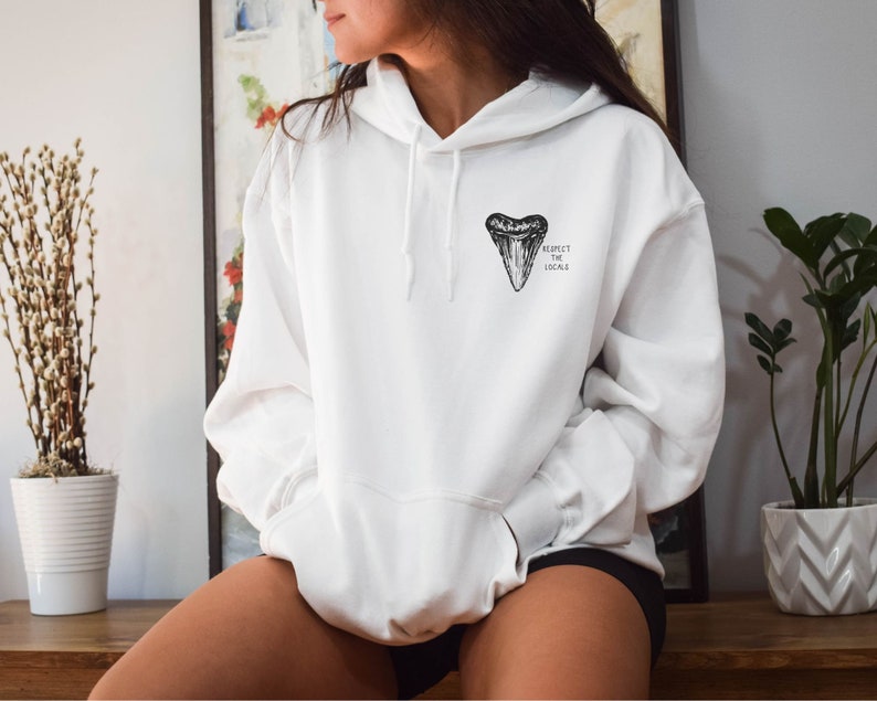 May include: White hoodie with a black shark tooth graphic and the text "Respect the Locals" printed on the front.