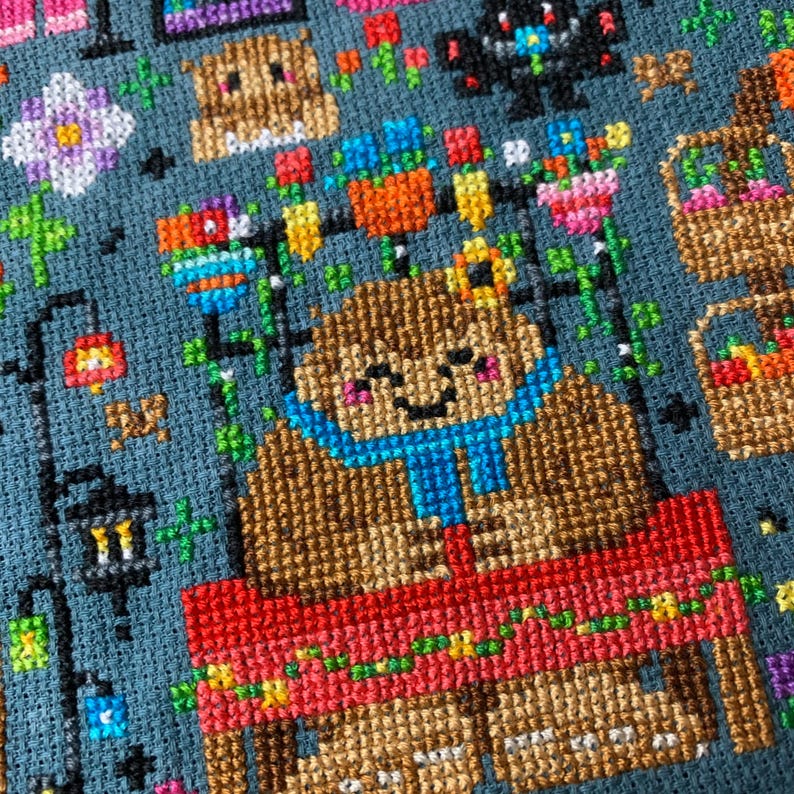 May include: A brown bear wearing a blue scarf sits at a red table with a colorful tablecloth. The bear has a happy expression on its face. The table is surrounded by flowers and other decorations.