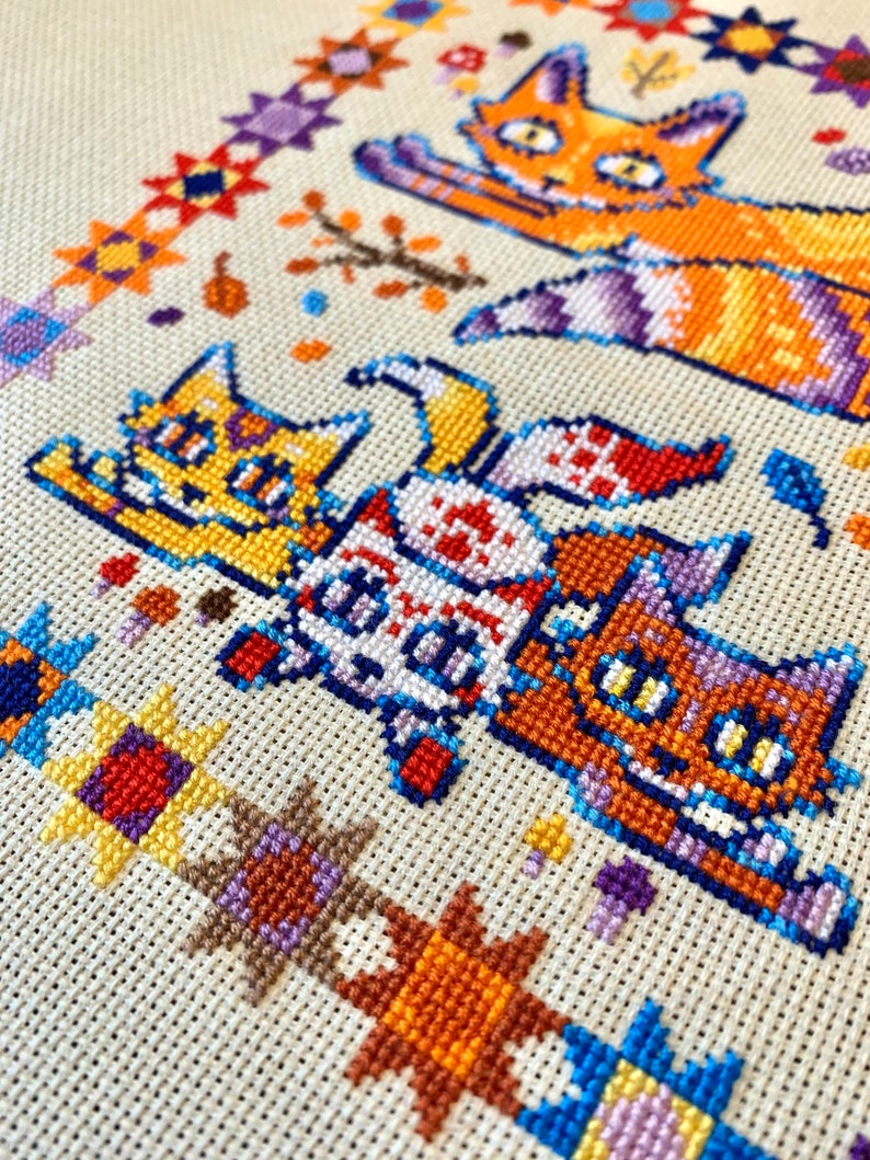 Puede incluir: Bordado de punto de cruz con cuatro gatos de pelaje naranja, amarillo, blanco y marr&oacute;n. Los gatos est&aacute;n dispuestos en fila, con el gato de arriba mirando hacia la derecha y los otros tres mirando hacia la izquierda. El fondo es una tela beige con un borde colorido de formas geom&eacute;tricas.