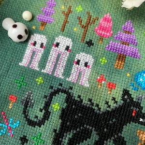 May include: Cross-stitch embroidery featuring a black wolf with a red eye, surrounded by white ghosts and colorful trees on a green background.