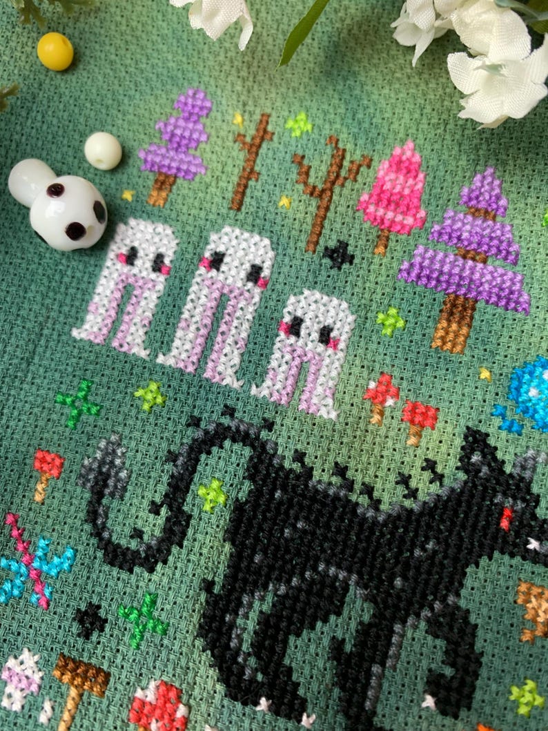 May include: Cross-stitch embroidery featuring a black wolf with a red eye, surrounded by white ghosts and colorful trees on a green background.
