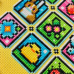 May include: A colorful cross-stitch pattern with a yellow background. The pattern features a variety of animals and objects, including a chick, a butterfly, a ladybug, and a flower. The pattern is framed in a black and white border.