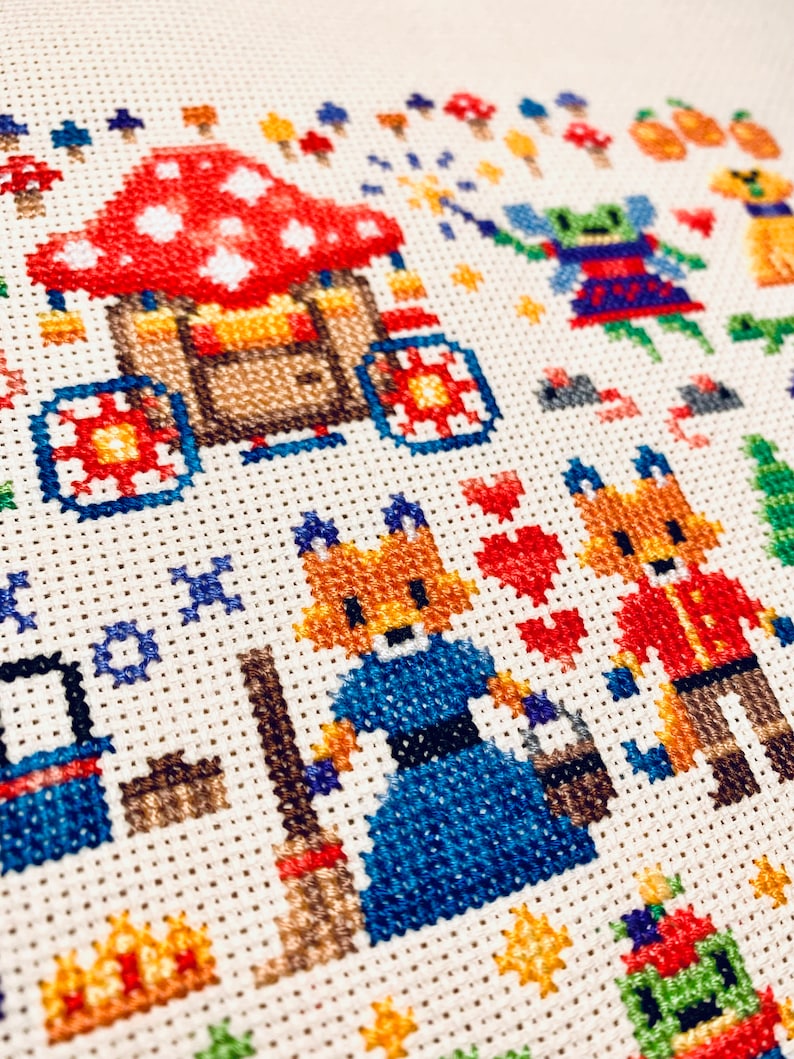 May include: Cross-stitch embroidery featuring a whimsical scene with a red and white mushroom house, two foxes, one holding a broom, and a green fairy with a wand. The background includes a variety of colorful mushrooms and stars.