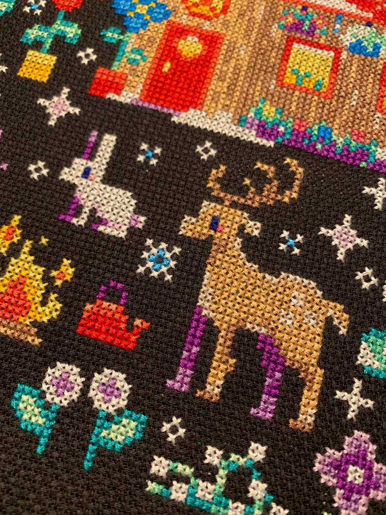 May include: A black cross-stitch design featuring a white rabbit, a brown reindeer, and various flowers and plants. The background is black with white stars.