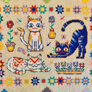 May include: A cross-stitch embroidery featuring three cats. The cats are a white and yellow cat with a red collar, a blue and white cat with a yellow collar, and a white and red cat with a green collar. The cats are surrounded by a colorful border of stars and flowers.