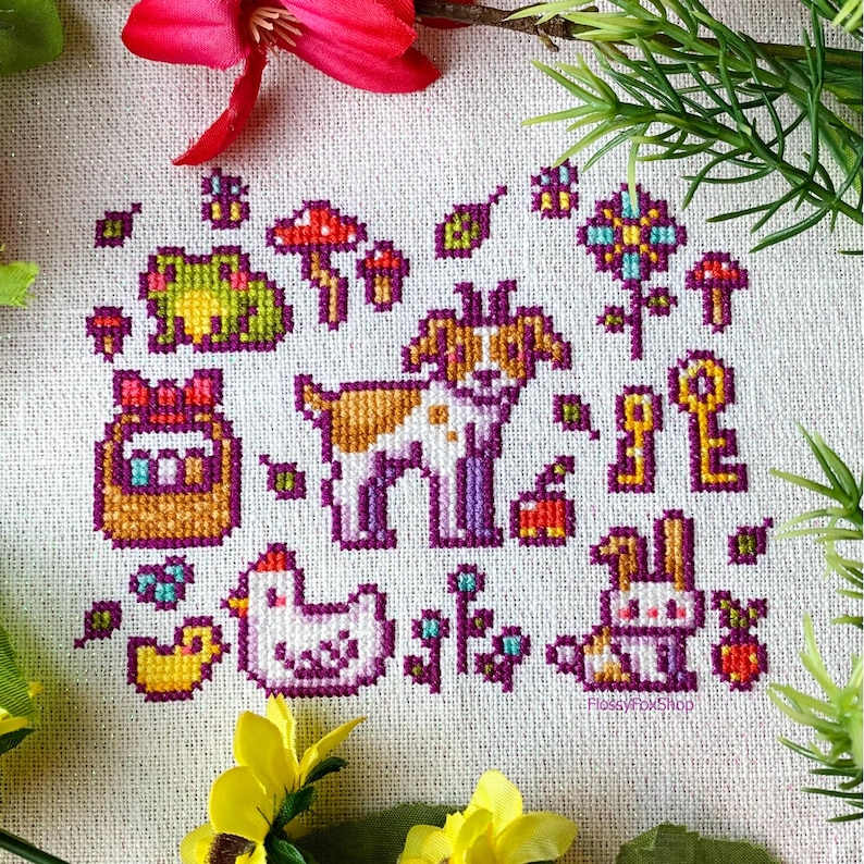K&ouml;nnte beinhalten: Kreuzstichmuster mit verschiedenen Tieren und Objekten, darunter ein Hund, ein Kaninchen, ein Frosch, ein Huhn, ein Korb mit Eiern, Pilze, Schl&uuml;ssel und Blumen. Das Muster ist auf wei&szlig;em Aida-Stoff mit bunten F&auml;den gestickt.